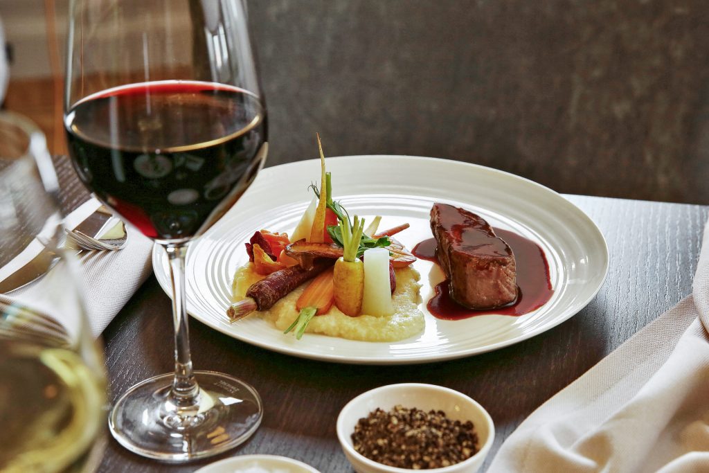 Meat with potatoes and vegetables served with red wine on restaurant table