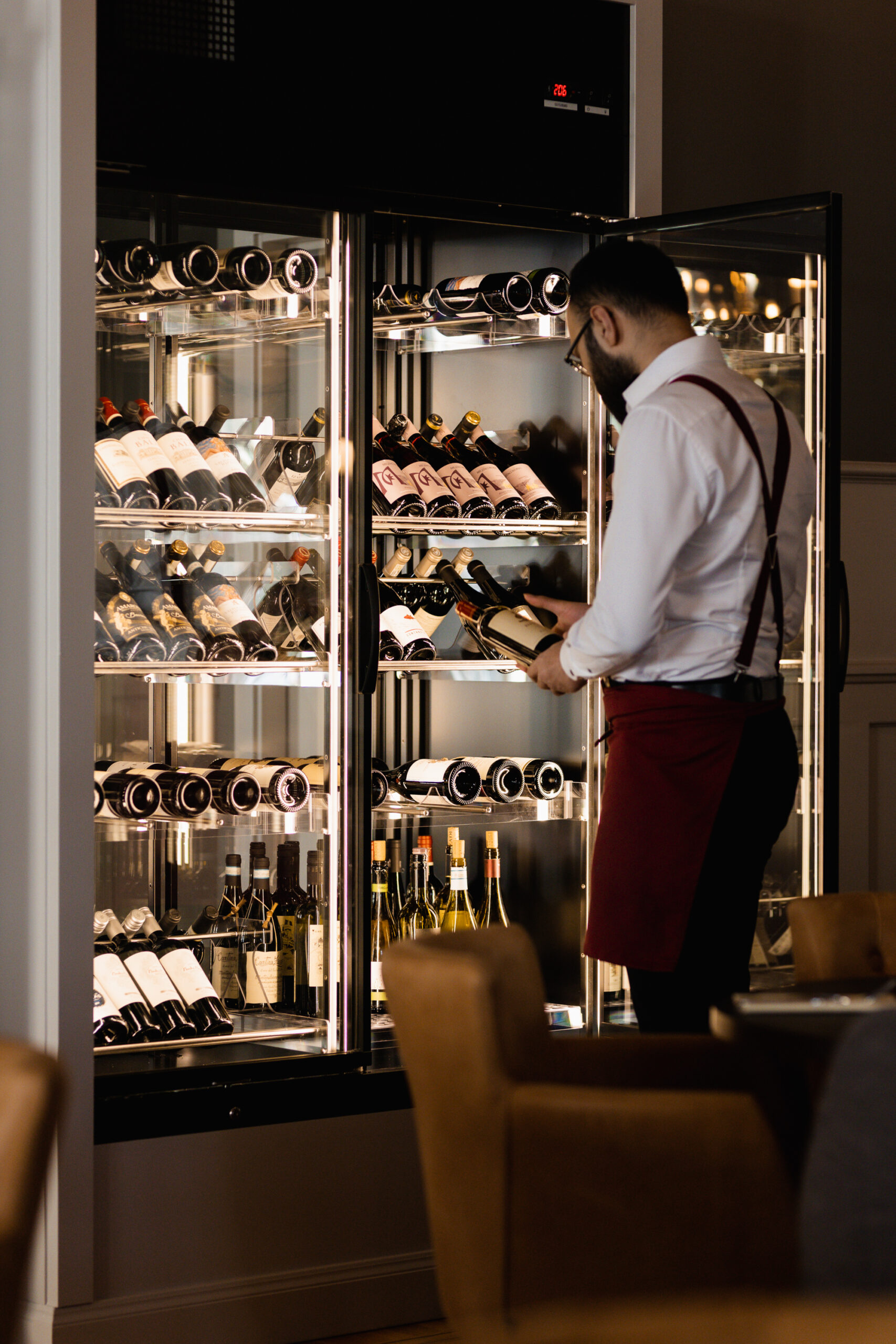 Sommelier väljer vin från belyst vinskåp med flaskor på hyllor