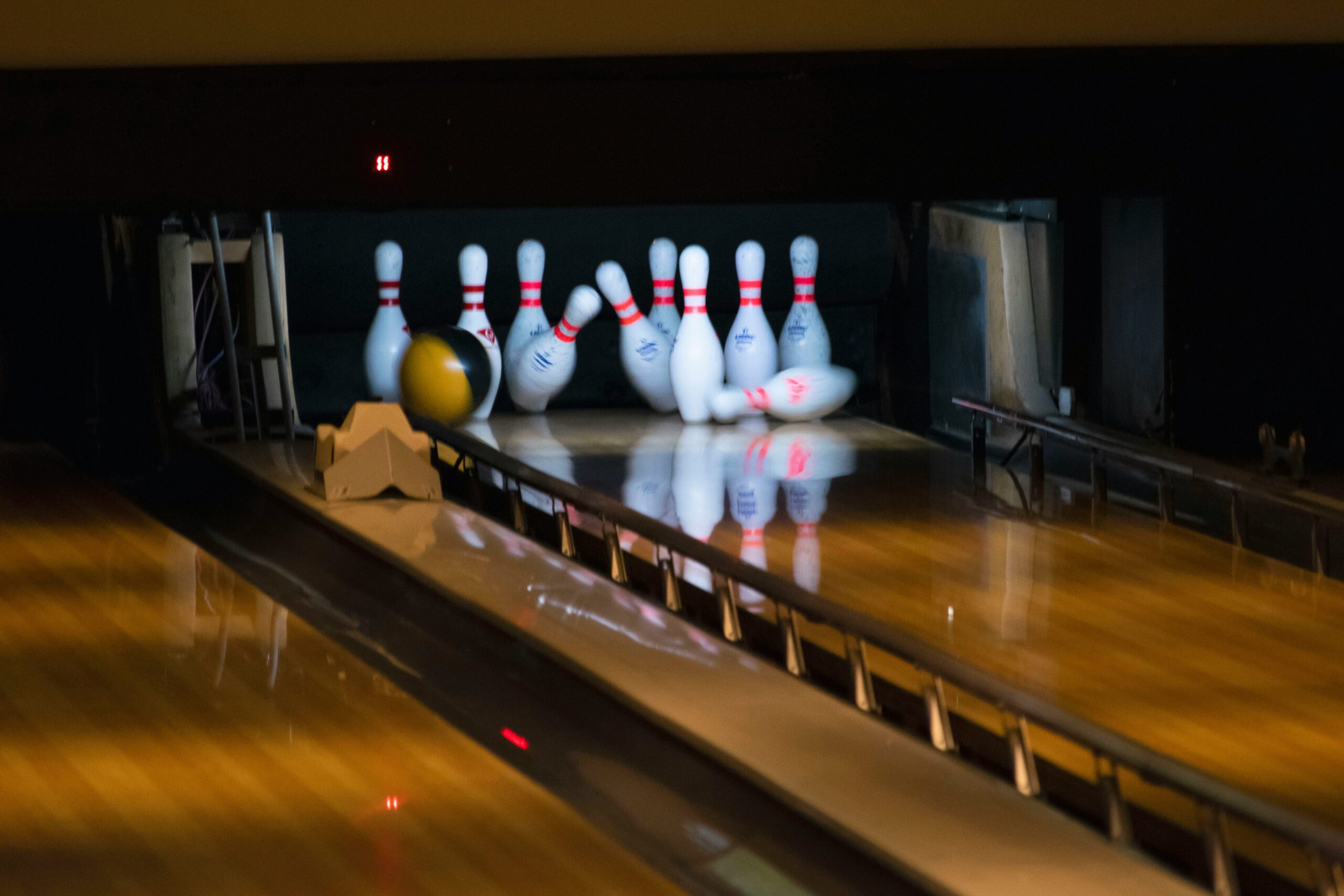 Bowlingkäglor på bowlingbana med bowlingklot i rörelse