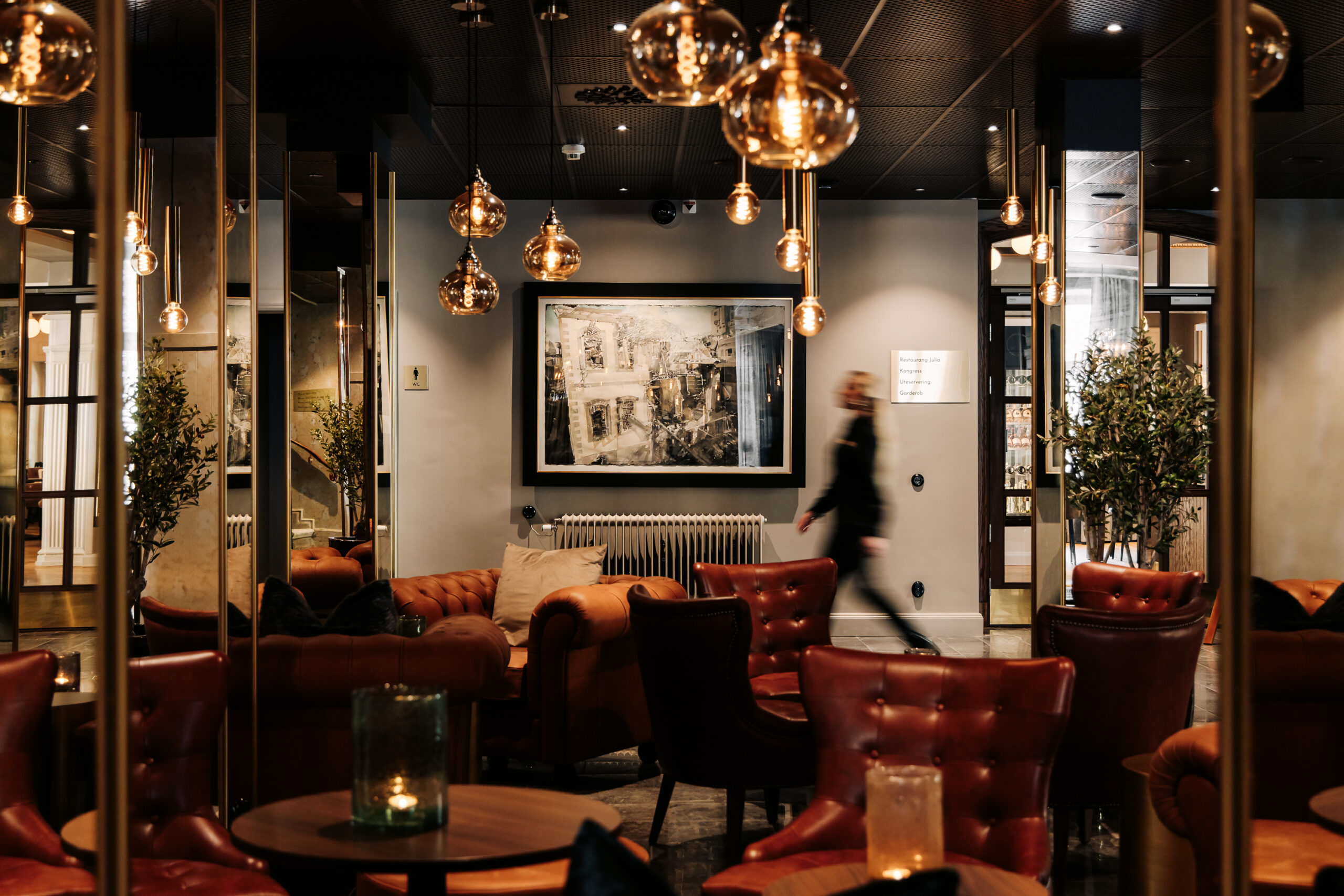 Elegant hotelllounge med bruna läderfåtöljer, gyllene lampor och konst på väggarna